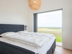 A bedroom with a large bed, a headboard, a wall-mounted light, and a view of a green landscape through a large window. - 5 Star Holiday Home in Lemvig (Lemvig)