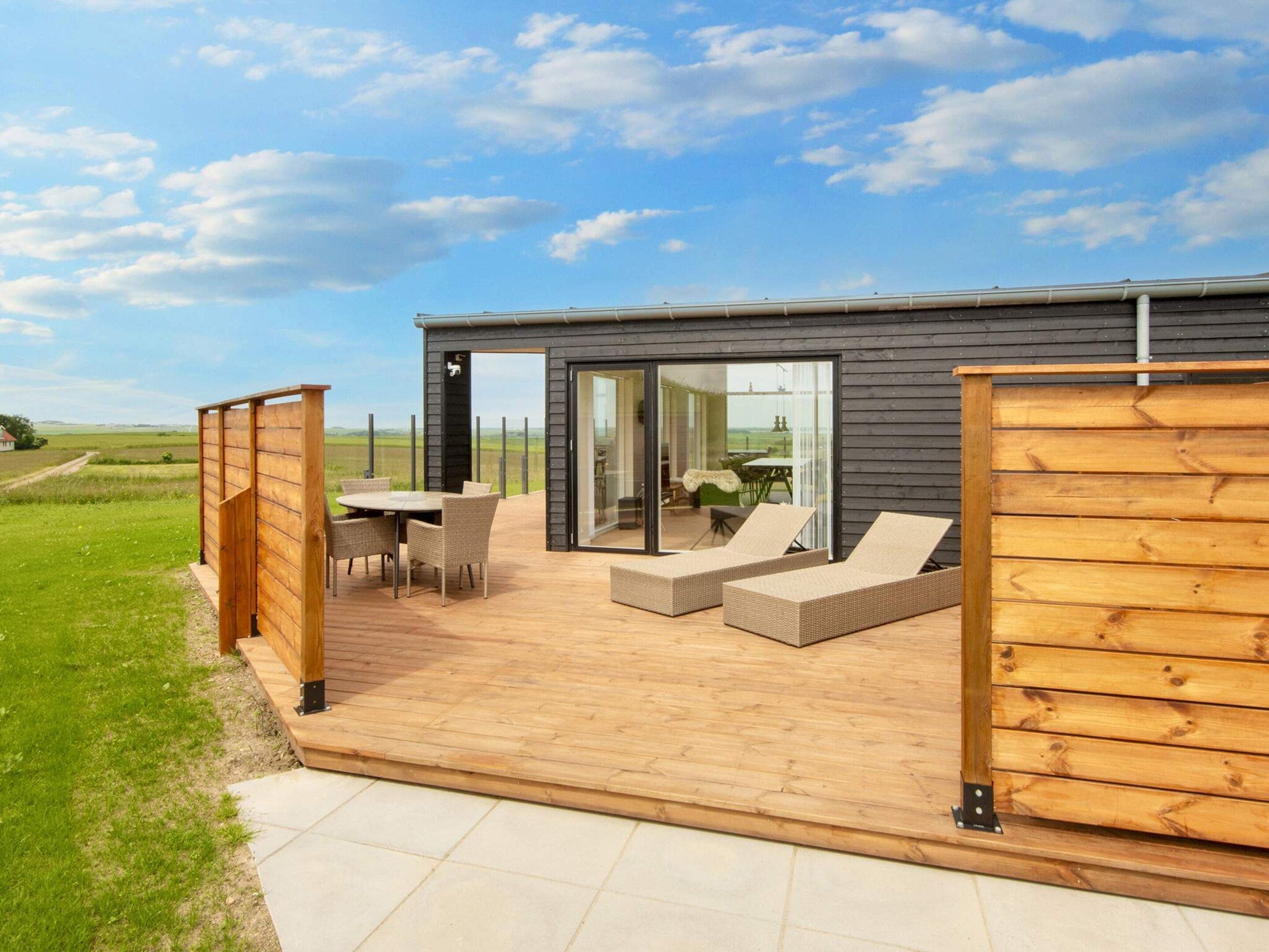 A modern outdoor patio with a dining table and chairs, a lounge area with cushions, and a glass door leading to an interior space.
