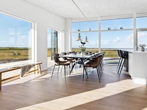 A modern dining area with a large table, chairs, and a view of the countryside through large windows. - 5 Star Holiday Home in Lemvig (Lemvig)