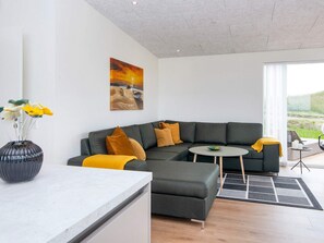 A modern living room with a grey sectional sofa, a small round table, and a vase with flowers. - 5 Star Holiday Home in Lemvig (Lemvig)