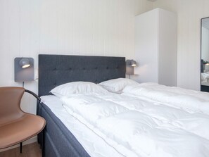 A neatly made bed with a grey headboard, two bedside lamps, and a brown chair in a hotel room.