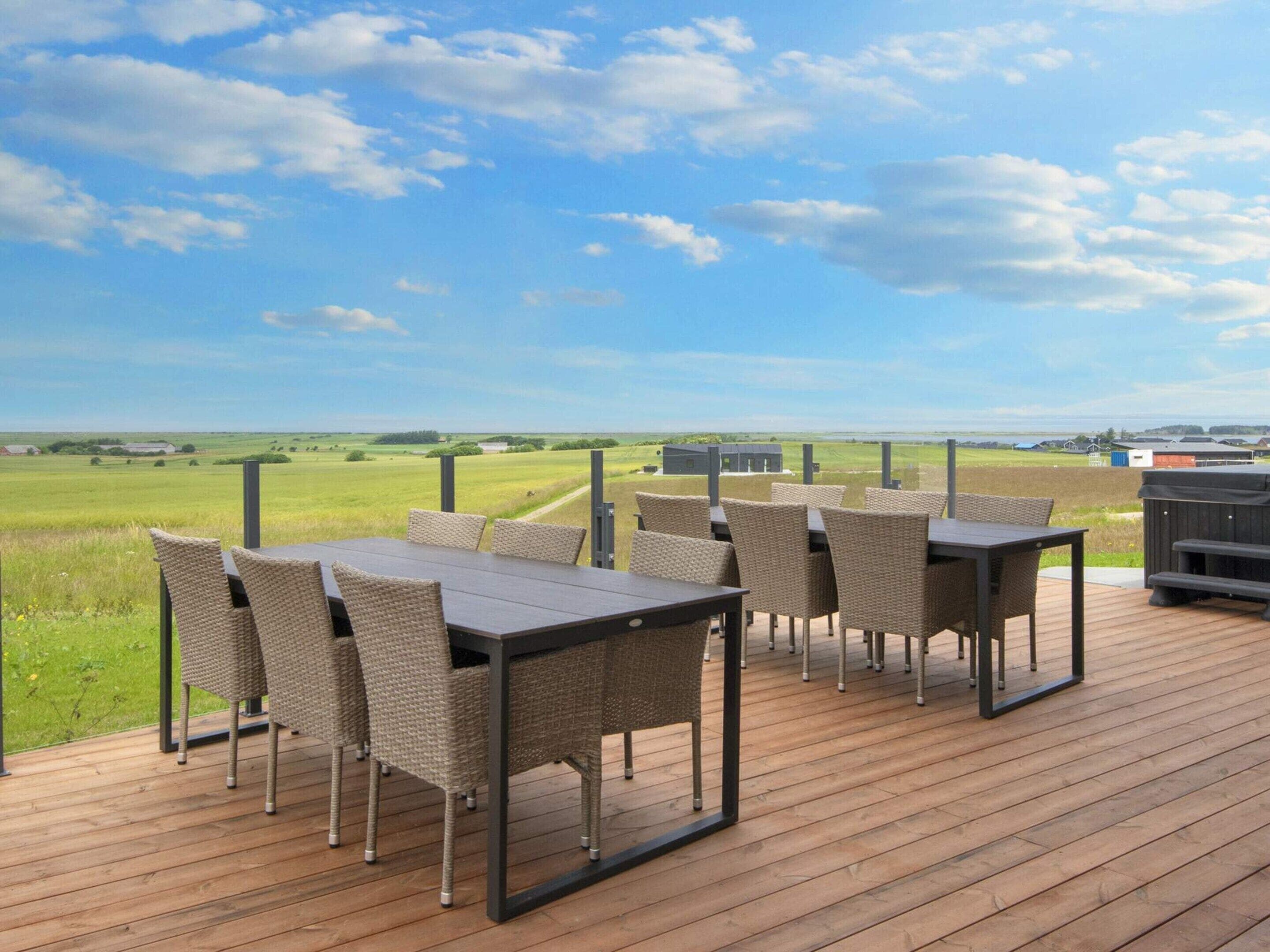 An outdoor deck with tables and chairs, overlooking a grassy field and distant buildings.
