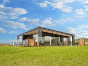 A modern building with large glass windows, a flat roof, and a grassy field in the foreground. - 5 Star Holiday Home in Lemvig (Lemvig)