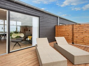 A modern outdoor seating area with wicker loungers, a wooden deck, and a glass door leading to an interior space with a view. - 5 Star Holiday Home in Lemvig (Lemvig)