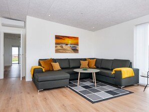 A modern living room with a sectional sofa, a small round table, and a large painting of a sunset. - 5 Star Holiday Home in Lemvig (Lemvig)