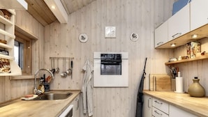 A kitchen with wooden panel walls, a built-in oven, a sink with a faucet, and a hanging rack with utensils. - 6 Person Holiday Home in Karrebaeksminde (Karrebæksminde)