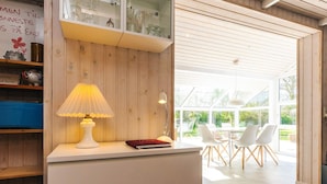 A modern interior with a wooden wall, a white desk with a lamp, and a view of an outdoor patio with chairs. - 6 Person Holiday Home in Karrebaeksminde (Karrebæksminde)