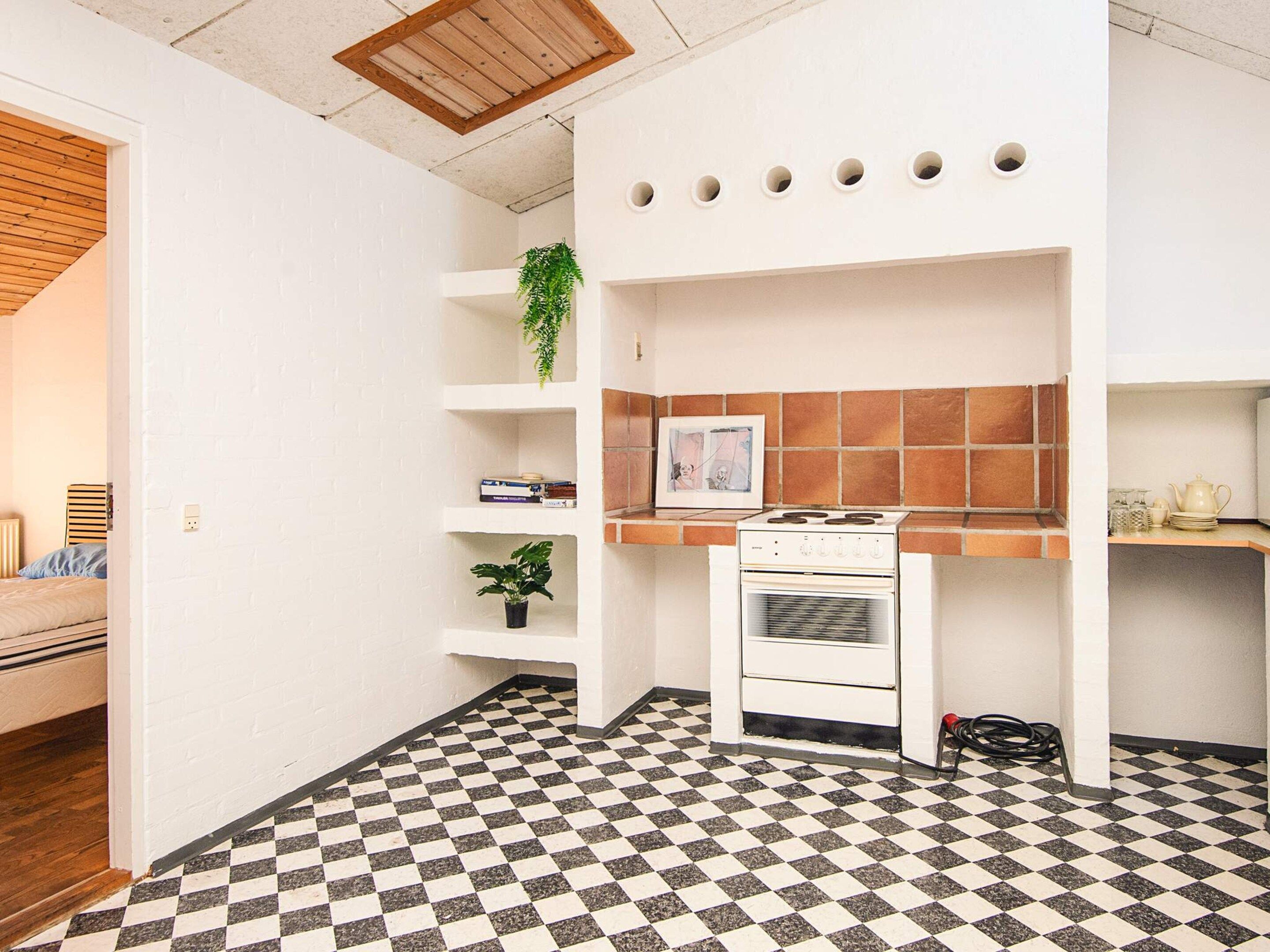 A compact kitchen with a checkered floor, a stove, and a shelf with a plant.