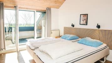 Un dormitorio con una cama grande, un cabecero con listones horizontales, una ventana con cortinas y un radiador.