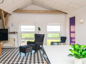 A room with a black and white checkered floor, two windows with views of greenery, a black armchair, a white table, and a potted plant. - 20 Person Holiday Home in Karby (Øster Assels)