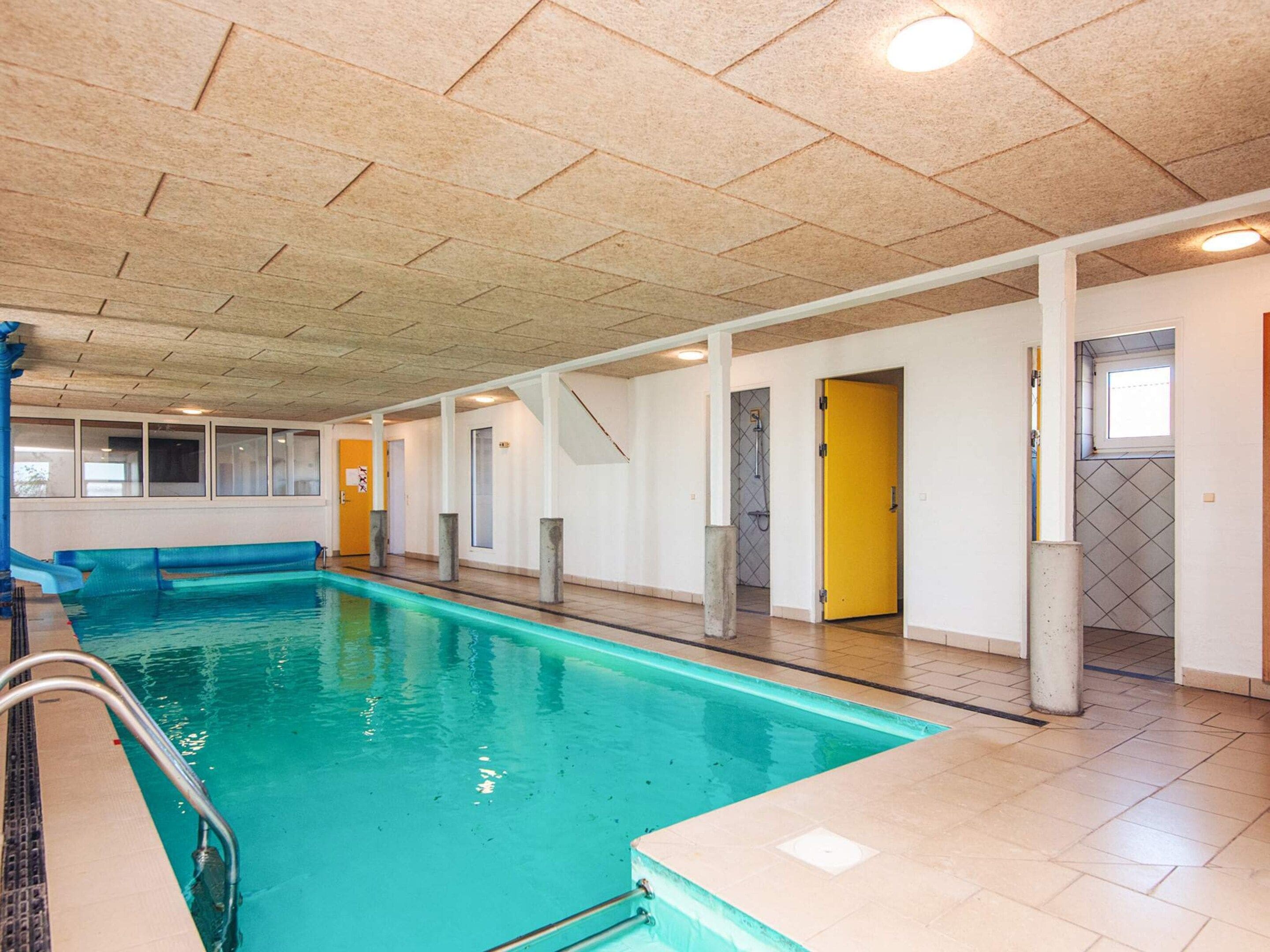An indoor swimming pool with clear water, surrounded by white walls and a tiled floor.