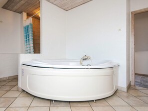 Een moderne badkamer met een groot, wit ligbad, een douchegedeelte en een houten plafond.