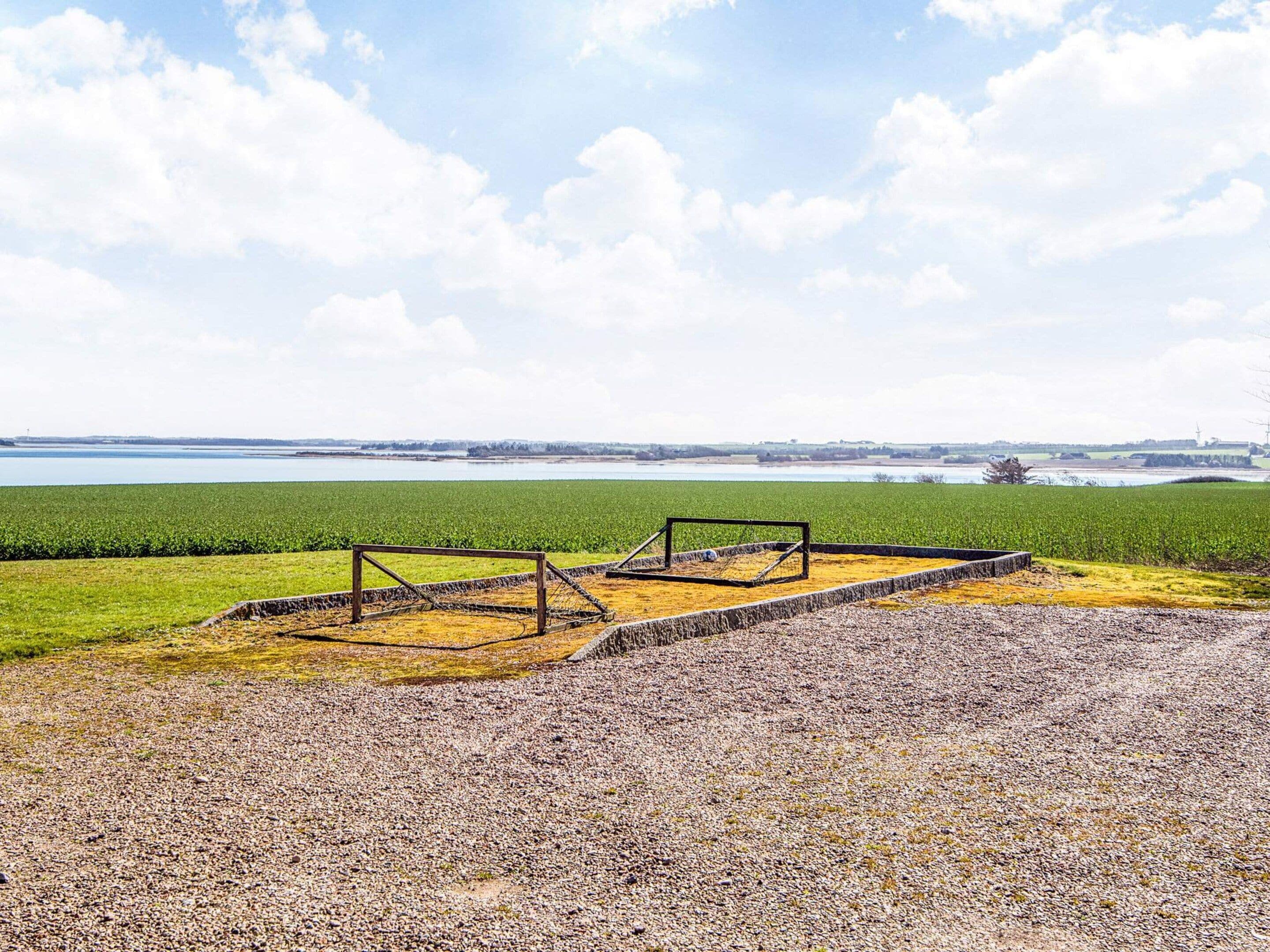Ein Kiesplatz mit einer Metallkonstruktion, einem grünen Feld und weiter Wasserfläche.