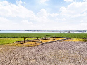 A gravel area with a metal structure, a green field, and a distant body of water. - 20 Person Holiday Home in Karby (Øster Assels)