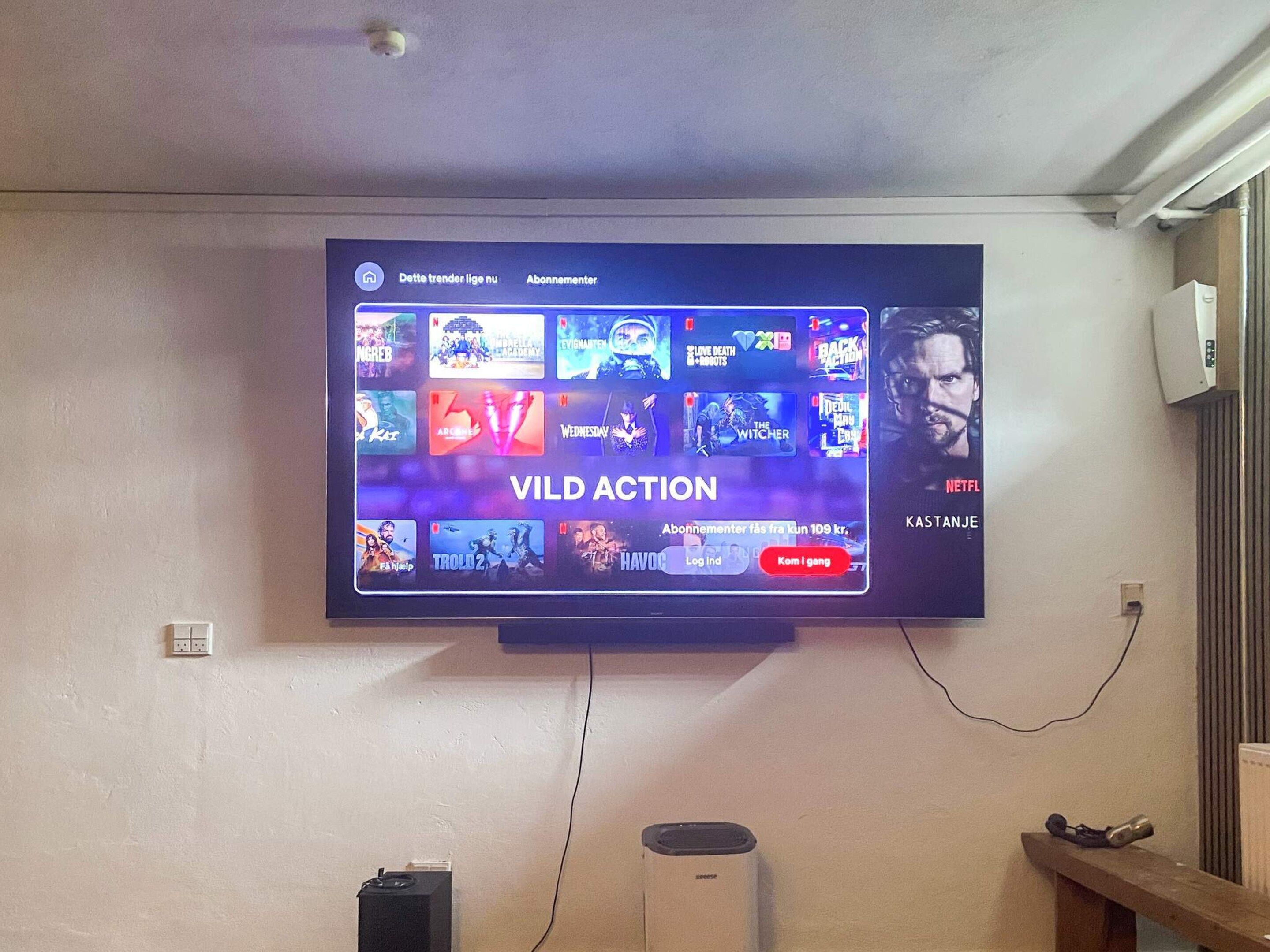 Ein an der Wand befestigter Fernseher zeigt eine Streaming-Oberfläche mit verschiedenen Sendervorschauen.