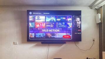 Uma televisão presa na parede exibindo a interface de um serviço de streaming, com diversas miniaturas de programas.
