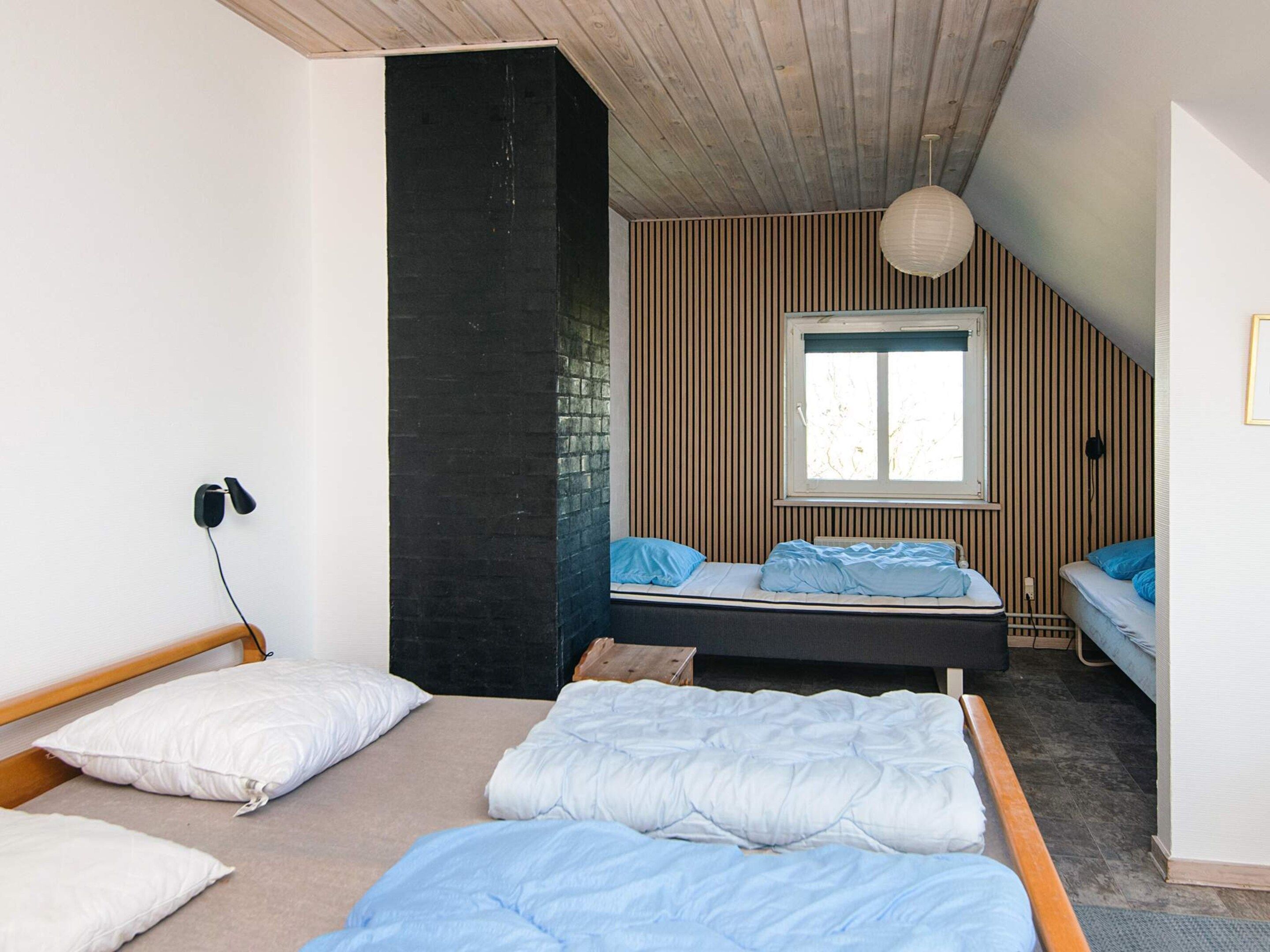 A bedroom with two beds, a window, and a wooden ceiling.
