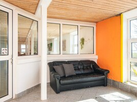 A room with a black leather sofa, large windows, and an orange wall.