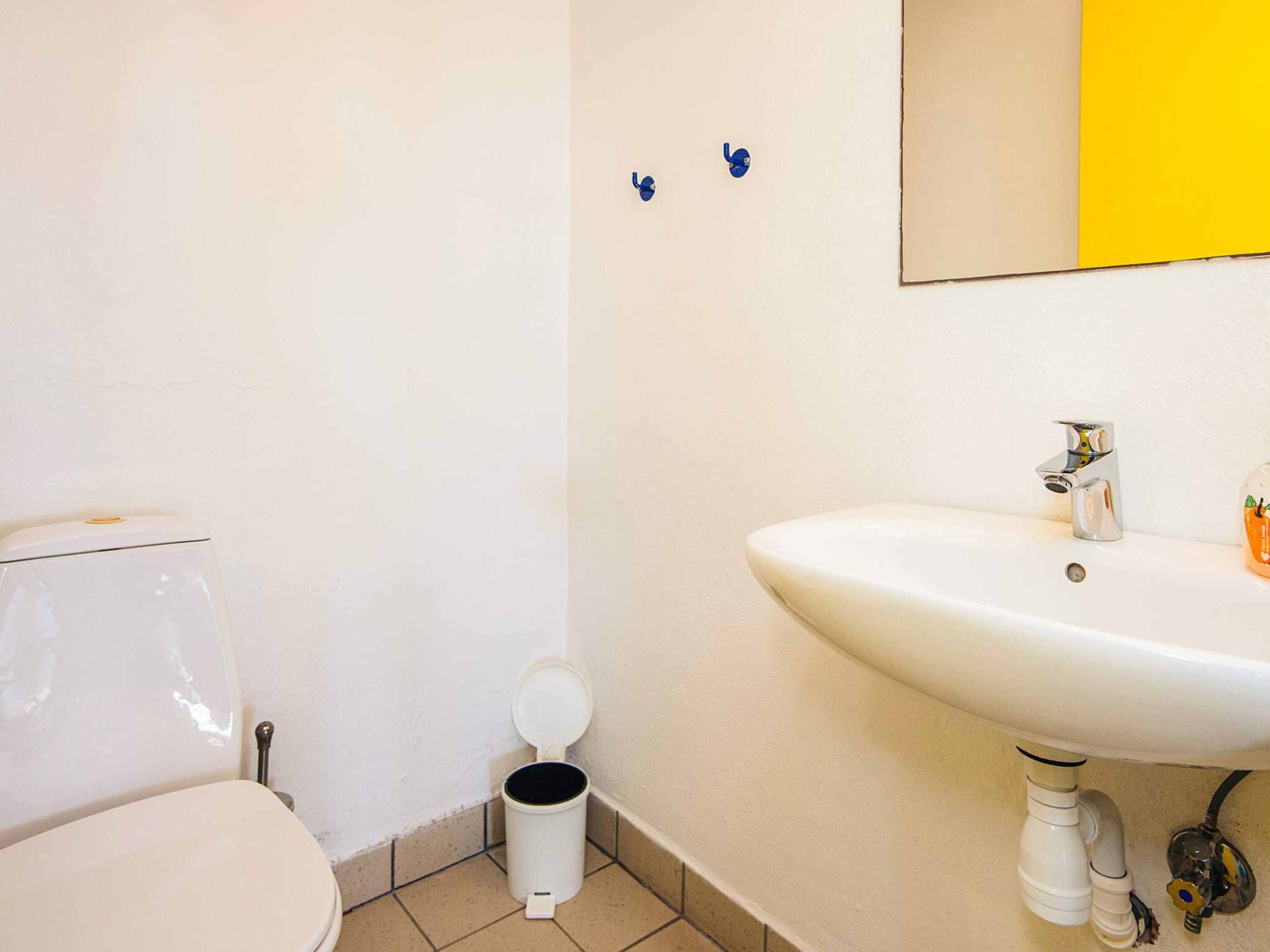 A bathroom with a toilet, a sink, and a trash bin.