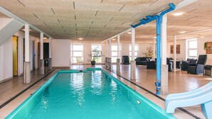 An indoor swimming pool with clear water, surrounded by lounge chairs and a seating area with a view of the pool. - 20 Person Holiday Home in Karby (Øster Assels)