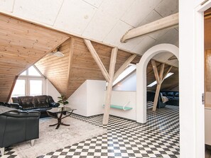 A loft-style room with a high ceiling, exposed wooden beams, a checkered floor, a leather sofa, and a glass table. - 20 Person Holiday Home in Karby (Øster Assels)