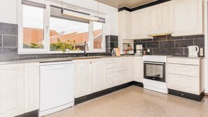 A modern kitchen with white cabinetry, a dishwasher, a stove, and a window overlooking a residential area. - 20 Person Holiday Home in Karby (Øster Assels)