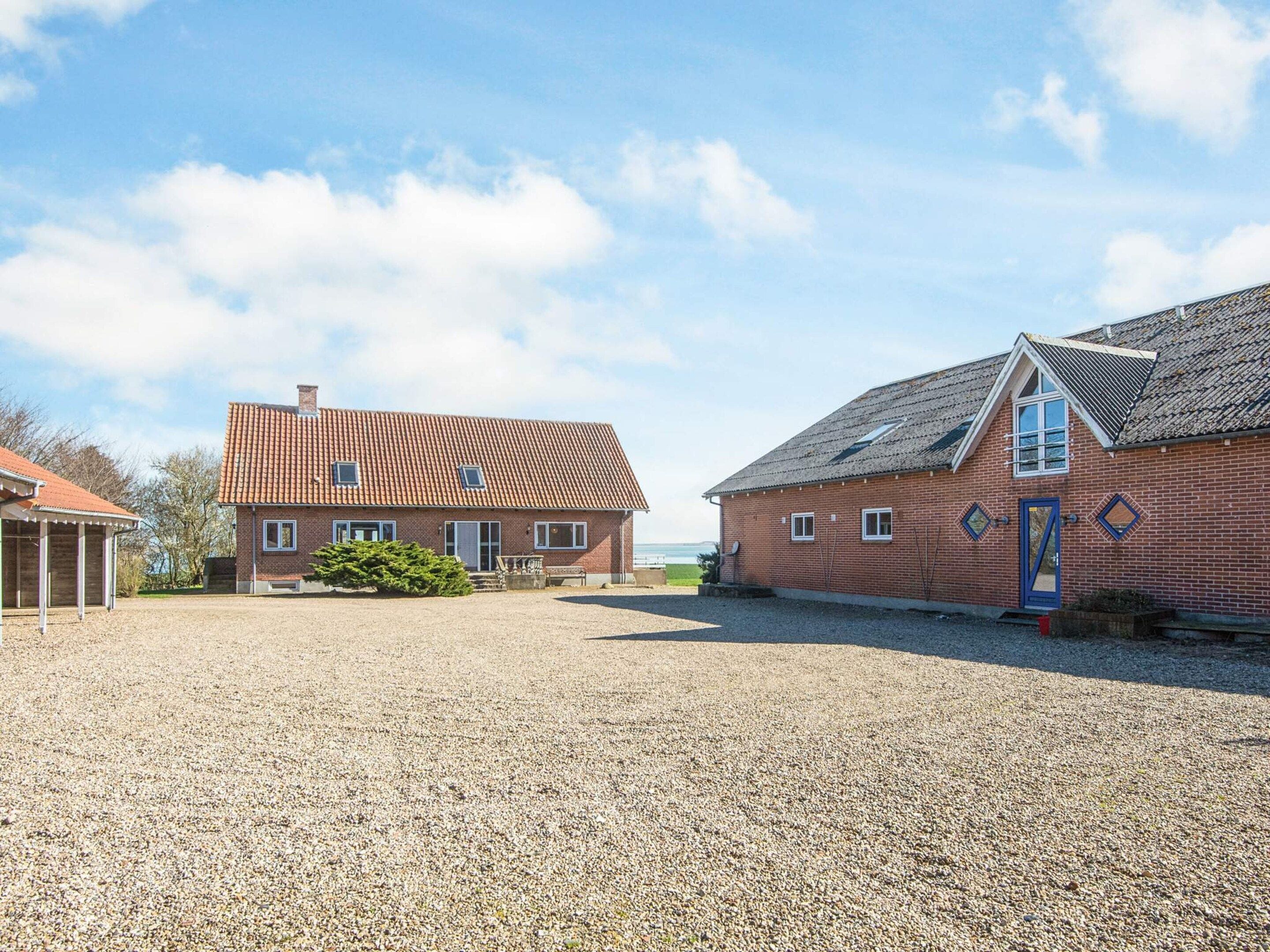 A gravel driveway leading to a brick building with a red-tiled roof and a blue door.