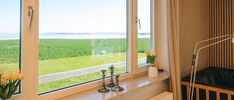 A room with a large window, a radiator, a bedside table with a lamp, and a view of a green field.
