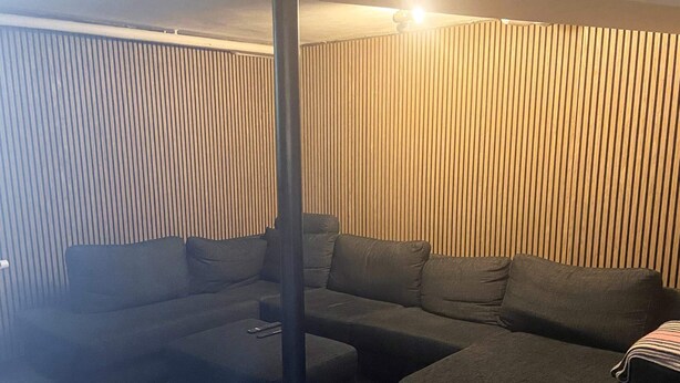 A living room with a sectional sofa, ottomans, and a tall black pillar. - 20 Person Holiday Home in Karby (Øster Assels)