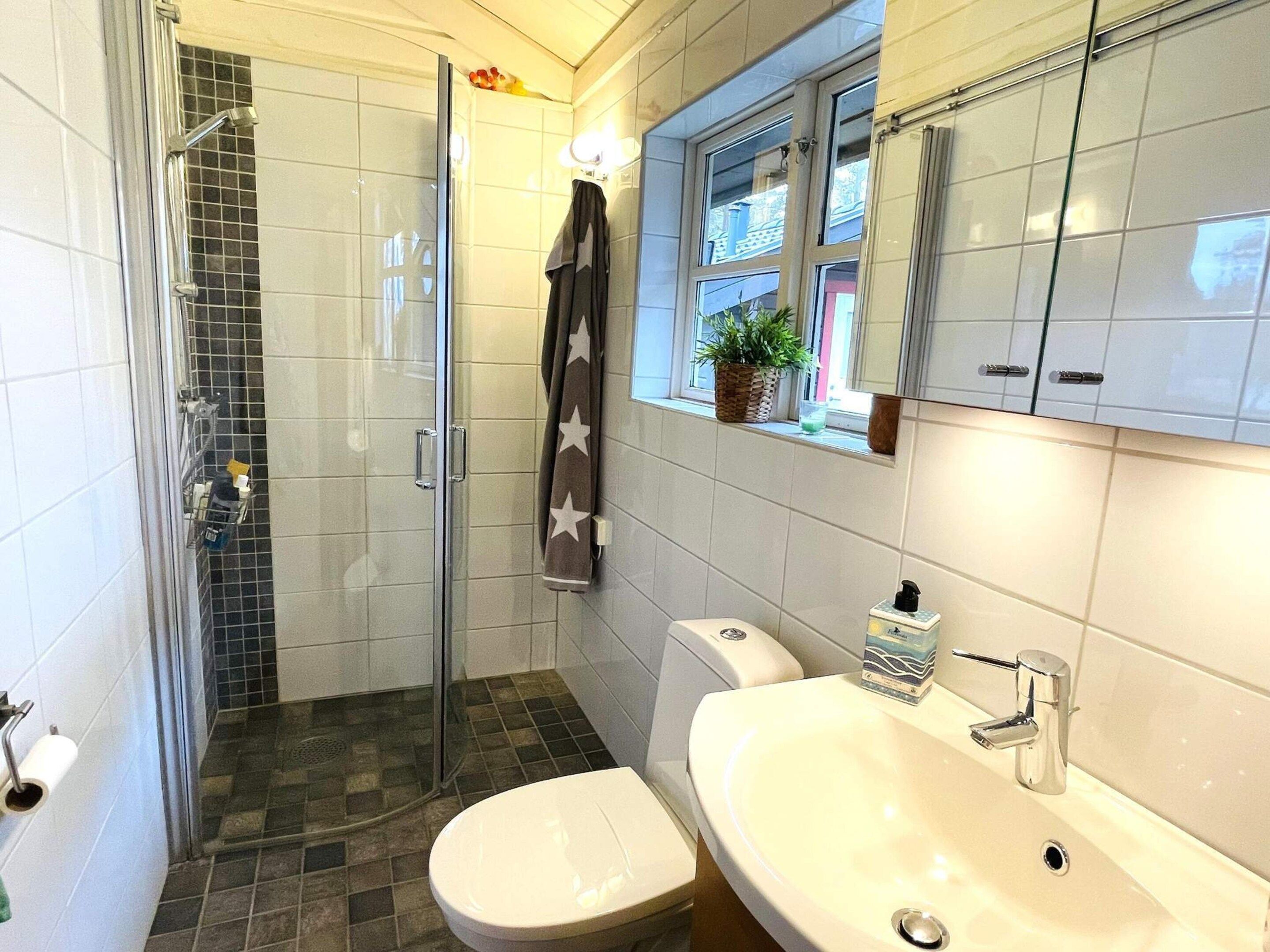 Une salle de bain équipée d’une douche, de toilettes, d’un lavabo et d’une fenêtre avec une plante.