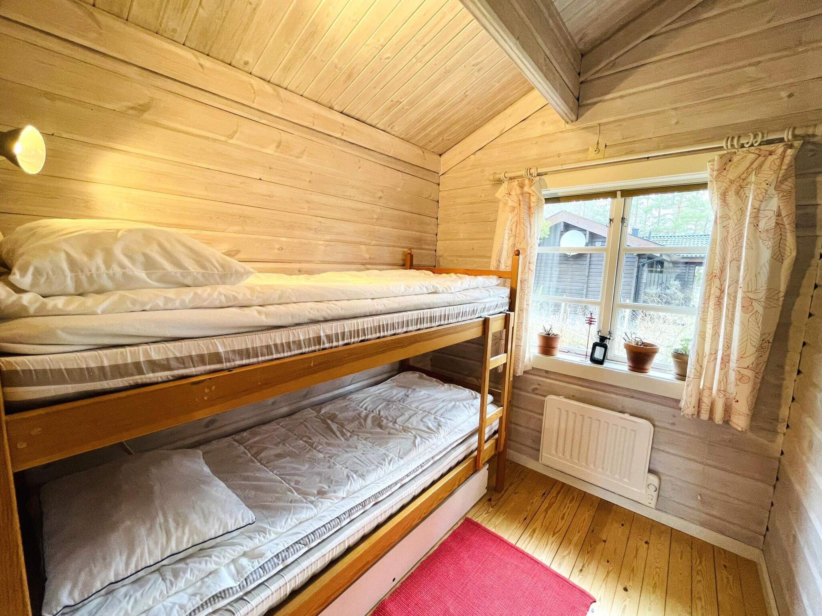 A bunk bed room with wooden walls, a window with curtains, and a radiator.