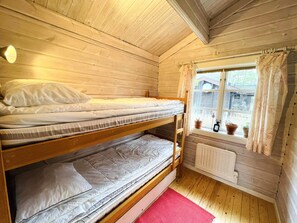A bunk bed room with wooden walls, a window with curtains, and a radiator. - 4 Star Holiday Home in Ronneby (Listerby)
