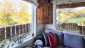 Une pièce chaleureuse avec un meuble en bois, un banc rembourré et une vue sur une terrasse en bois et des arbres.
