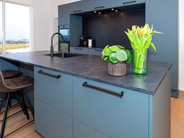 Cocina moderna con encimera oscura, un lavabo y horno empotrado. Hay dos taburetes y una planta en maceta sobre la encimera.