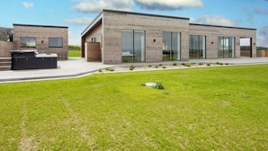 A modern two-story building with large sliding glass doors and a patio area with a hot tub. - 5 Star Holiday Home in Lemvig (Lemvig)
