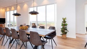 A modern dining area with a long table, multiple chairs, pendant lights, and a view through large windows. - 5 Star Holiday Home in Lemvig (Lemvig)
