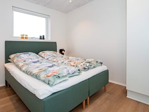 A bed with a floral bedspread, a bedside table with a lamp, and a window above the bed.