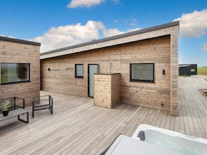 A modern building with a wooden exterior, a deck, and a hot tub.