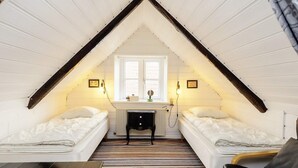 Une petite chambre à coucher de style mansardé, avec deux lits, un radiateur, un bureau et une fenêtre.