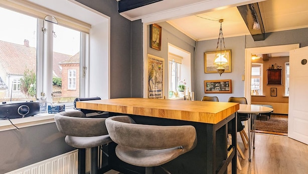 Une cuisine moderne avec un coin bar, deux tabourets de bar, un luminaire suspendu et une vue sur l’extérieur.