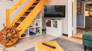 Un salon avec un escalier en bois, un téléviseur, une roue de navire et une télécommande posée sur une table en bois.