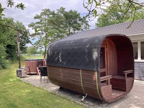 Une structure en forme de tonneau, faite de bois, avec un toit incurvé, un petit porche et une grille métallique au sol.