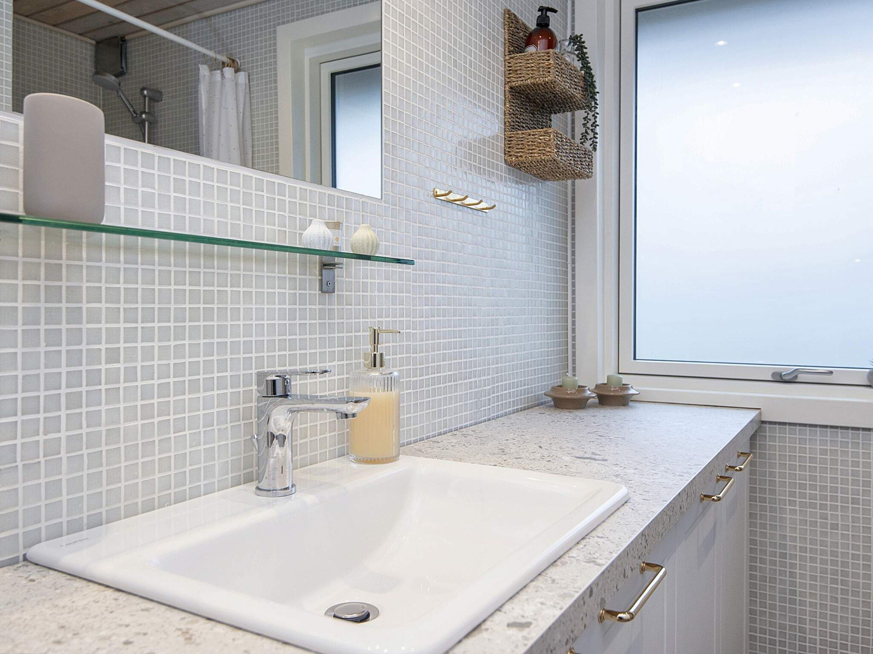 A bathroom with a white sink, a glass shelf with toiletries, and a window.