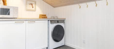 A laundry room with a washing machine, a microwave, and a wooden shelf with a bird.