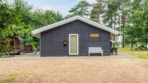 A small, dark wooden cabin with a white door and a bench outside. - 4 Star Holiday Home in Ansager (Ansager)