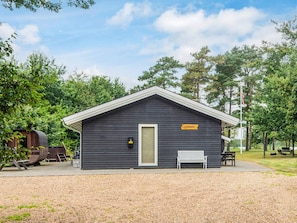 A small, dark wooden cabin with a white door and a bench outside. - 4 Star Holiday Home in Ansager (Ansager)