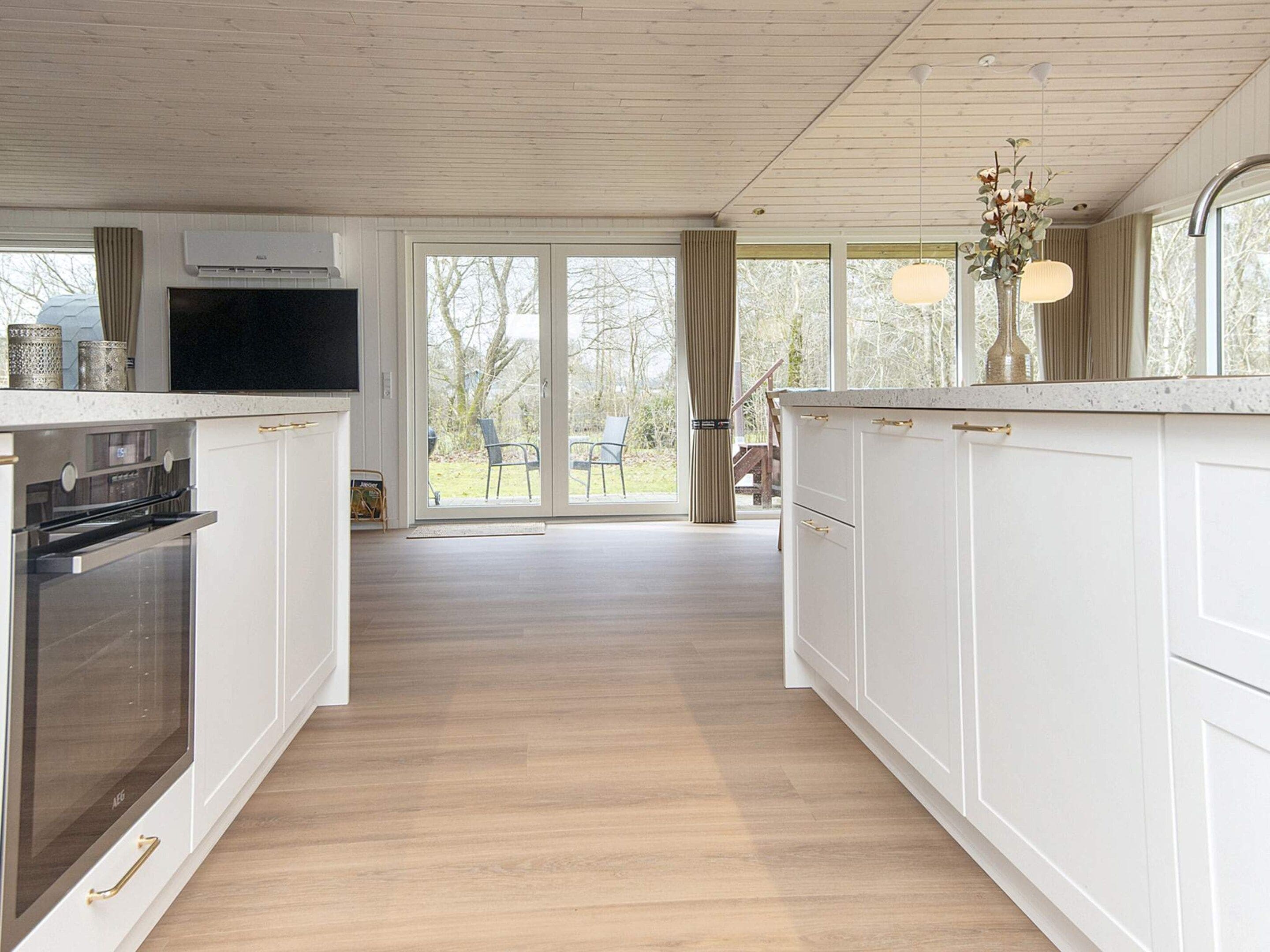 A modern kitchen with white cabinetry, a built-in oven, and a large window overlooking a deck.