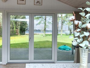 A room with a sliding glass door leading to a grassy outdoor area with trees and a body of water. - 4 Star Holiday Home in Ansager (Ansager)