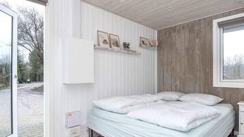 A bedroom with a bed, a bedside table, a window, and a door leading to an outdoor area.
