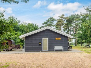 Eine kleine, dunkle Holzhütte mit einer weißen Tür und einer Bank davor.
